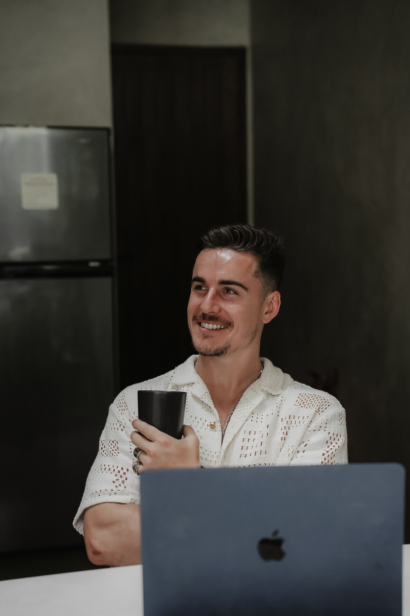 Jordan Candlish smiling without sunglasses, holding a coffee cup